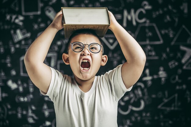 Un garçon avec des lunettes a étudié et a mis un livre sur sa tête dans la classe.