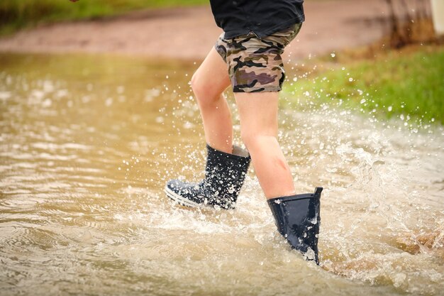 Garçon marchant dans un ruisseau inondé portant des bottes en caoutchouc