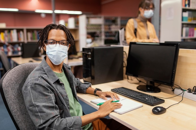 Photo gratuite garçon avec masque médical étudiant dans la bibliothèque