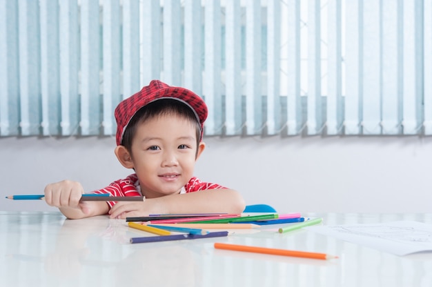Un garçon mignon dessine avec des crayons de couleur dans la chambre des enfants