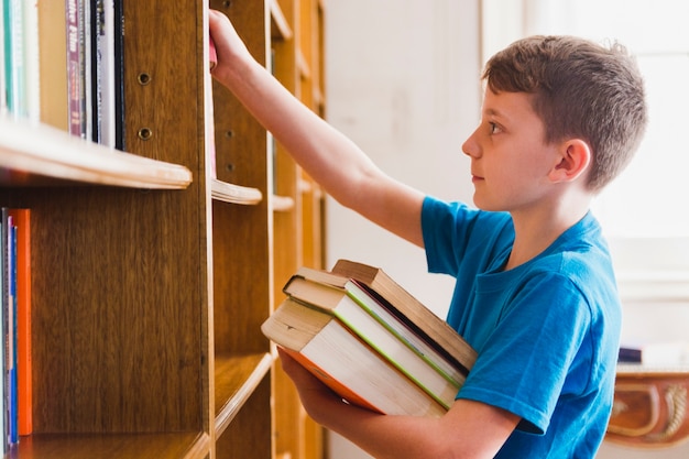 Garçon mignon prenant des livres choisis sur étagère