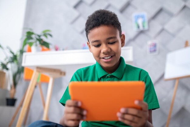 Garçon à la peau foncée regardant une tablette avec intérêt