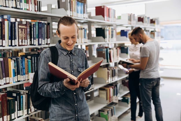 Garçon Pensif Ressemble à Un étudiant Debout Avec Un Livre Dans La Bibliothèque D'une Université Photo Premium