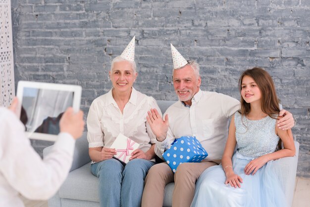Garçon prenant une photo de ses grands-parents et de sa soeur assis sur un canapé avec tablette numérique