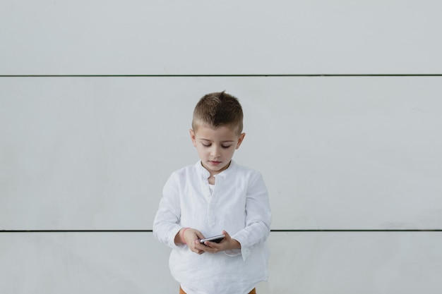 Garçon regardant vers le bas, jouant sur son téléphone avec un mur blanc