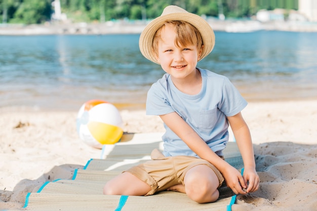 Garçon souriant assis sur un tapis au bord du sable