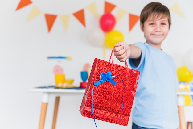 Photo gratuite garçon souriant, donnant un sac cadeau rouge à quelqu'un