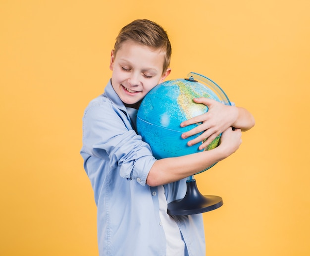 Garçon souriant embrassant la main du globe sur fond jaune