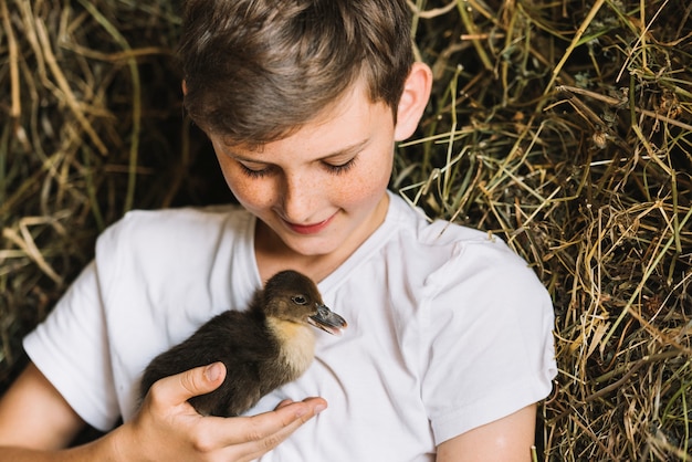 Photo gratuite garçon souriant en regardant canard devant le foin