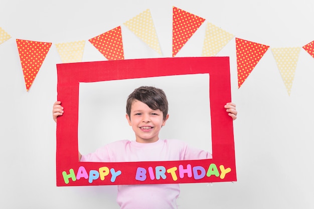 Garçon souriant tenant un cadre d&#39;anniversaire rouge en fête