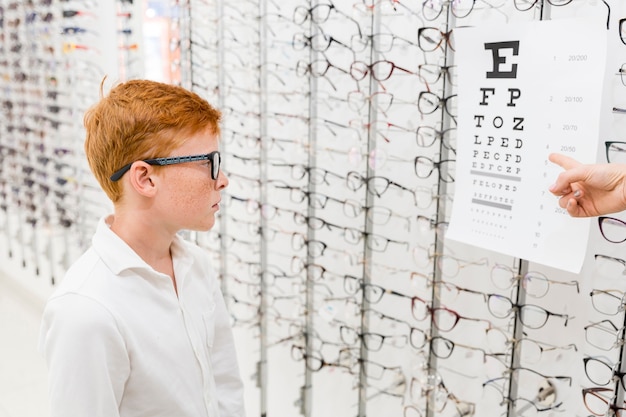 Garçon avec spectacle en regardant la carte de Snellen tandis que la main du docteur pointant sur la carte