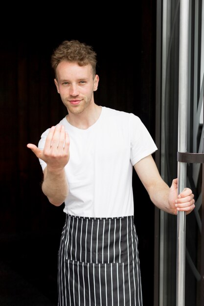 Garçon avec tablier vous invitant à l'intérieur du café