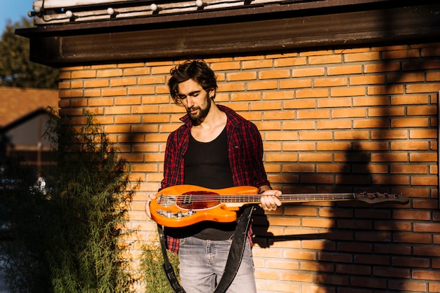 Garçon tenant la guitare électrique devant le mur de briques