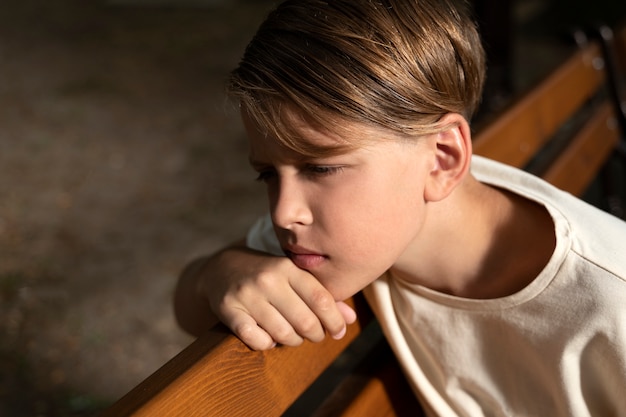 Photo gratuite garçon triste grand angle assis sur un banc