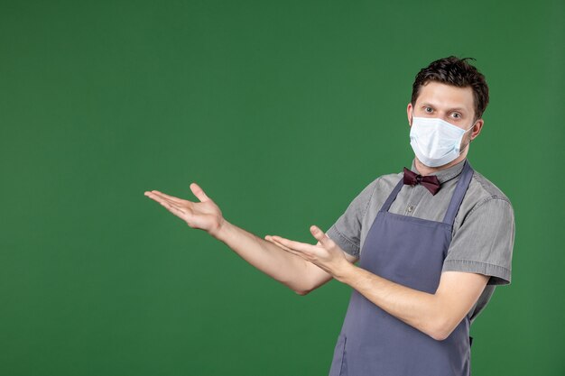 Photo gratuite garçon en uniforme avec masque médical et pointant vers le haut sur le côté droit sur fond vert