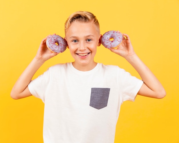 Garçon vue de face avec des beignets à ses oreilles