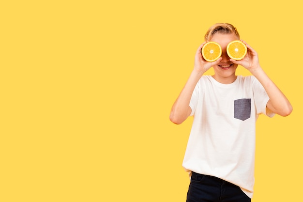 Photo gratuite garçon vue de face couvrant les yeux avec des tranches d'orange
