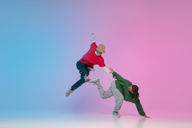 Garçons dansant le hiphop dans des vêtements élégants sur fond dégradé à la salle de danse à la lumière du néon