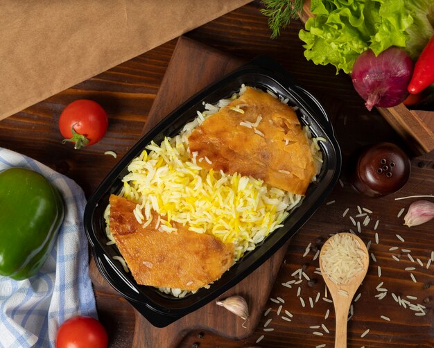 Garniture de riz, plats à emporter dans un récipient noir sur une planche en bois.