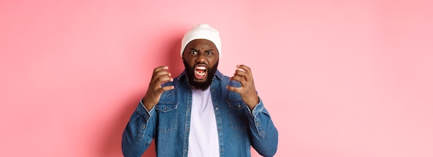 Photo gratuite un gars afro-américain en colère criant et regardant un cri énervé à la caméra debout sur un backgro rose