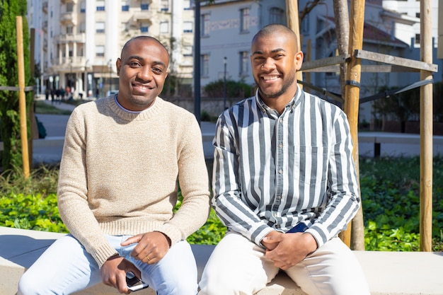 Photo gratuite gars afro-américains souriants assis sur un banc avec des téléphones