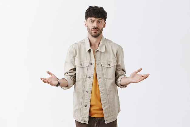 Gars barbu élégant confus posant contre le mur blanc