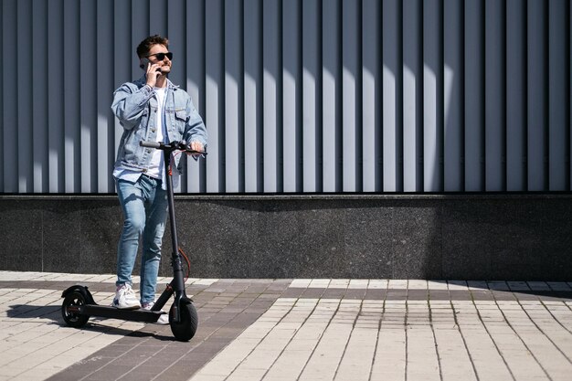 Le gars conduit un scooter électrique dans le contexte de la ville. u chanter téléphone.