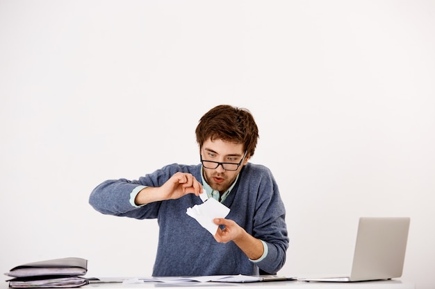 Un gars déchire des documents et regarde avec une expression curieuse et intéressée, s'amuse au travail, devient fou des délais