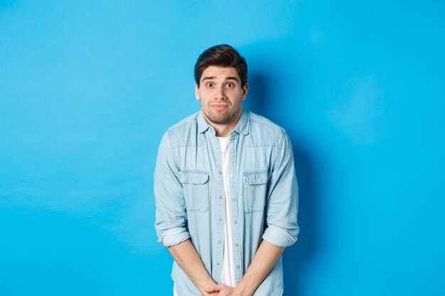 Un gars embarrassé veut faire pipi, fait la queue pour les toilettes, debout sur fond bleu.