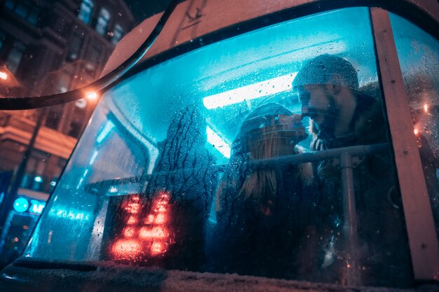 Le gars et la fille s'embrassent dans le tramway derrière le verre brumeux