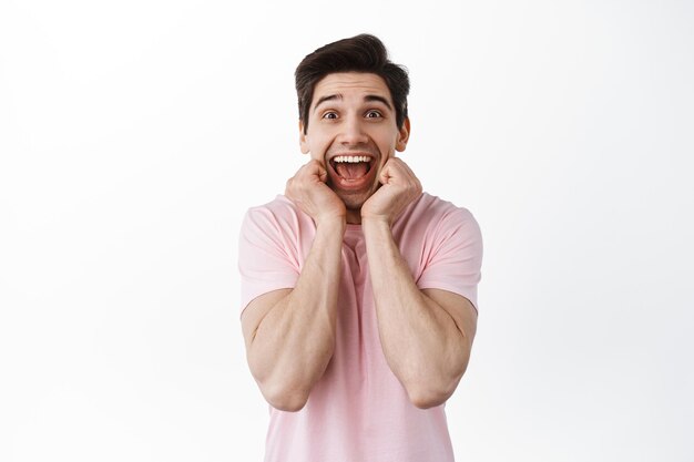 Un gars heureux et excité crie de joie et de bonheur, se tient la main sur le visage, se réjouit, gagne et célèbre, crie de plaisir, se tient sur fond blanc