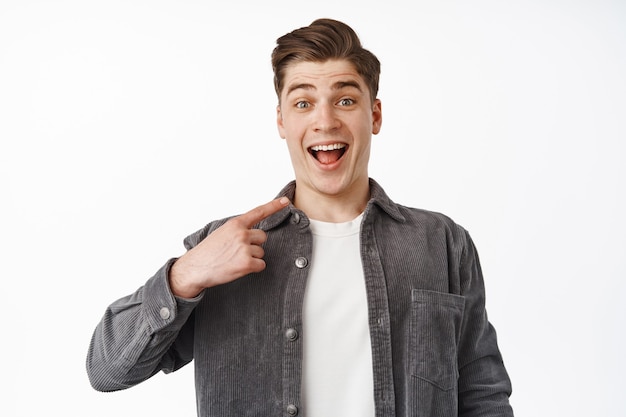 Un gars heureux surpris d'être choisi, pointant du doigt lui-même et souriant émerveillé, remportant quelque chose, célébrant, étant nominé, choisi, debout sur blanc