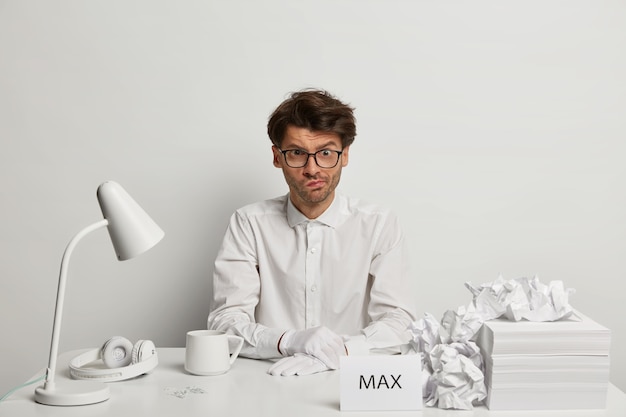 Photo gratuite un gars hipster embarrassé pose sur le lieu de travail, serre les lèvres et a l'air nerveux