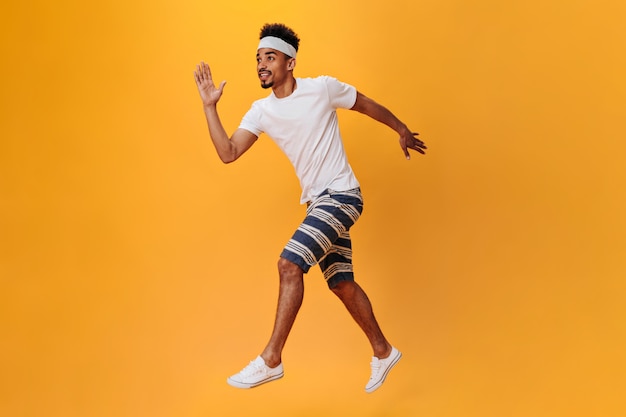 Un gars à la peau foncée en short et T-shirt court sur un mur orange. Le sportif a la séance d'entraînement sur d'isolement