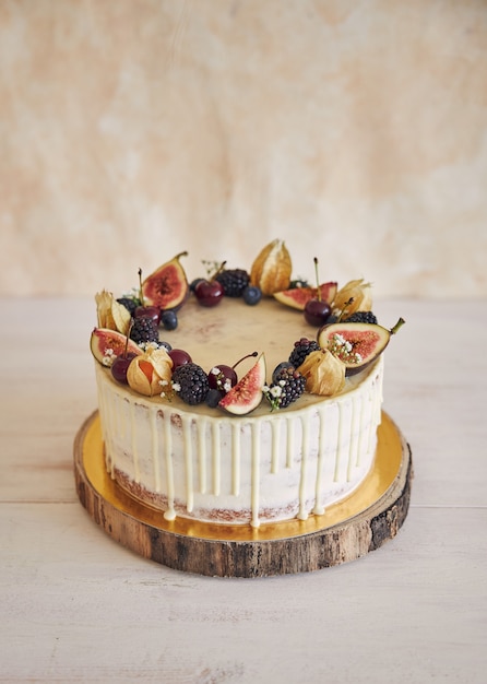 Un gâteau d'anniversaire fruité avec une décoration d'anniversaire, des fruits sur le dessus et une goutte blanche sur un mur beige