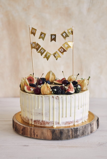 Un gâteau d'anniversaire fruité avec dessus d'anniversaire, fruits sur le dessus et goutte blanche sur fond beige