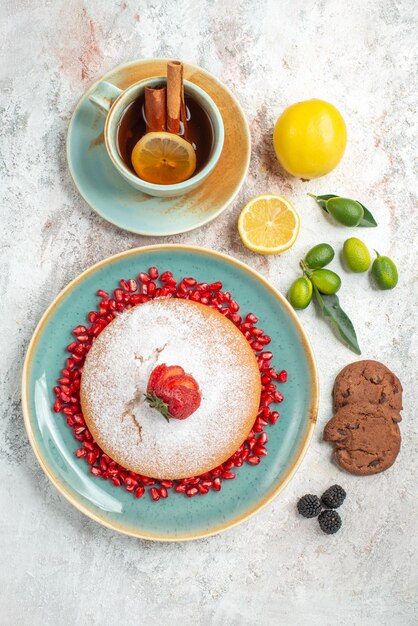 gâteau appétissant une tasse de thé à la cannelle et au citron à côté de l'assiette de gâteau avec des fraises et des graines de biscuits au chocolat à la grenade sur la table