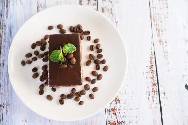 Photo gratuite gâteau au chocolat sur une plaque blanche avec des grains de café sur une table en bois