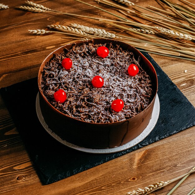 Un gâteau au chocolat vue de face décoré de cerises rond délicieux à l'intérieur de la casserole de gâteau brun anniversaire confiserie sucrée sur le fond brun