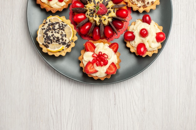 Gâteau au chocolat vue rapprochée demi-haut arrondi avec des tartelettes aux baies dans la plaque grise en haut au centre de la table en bois blanc avec espace copie