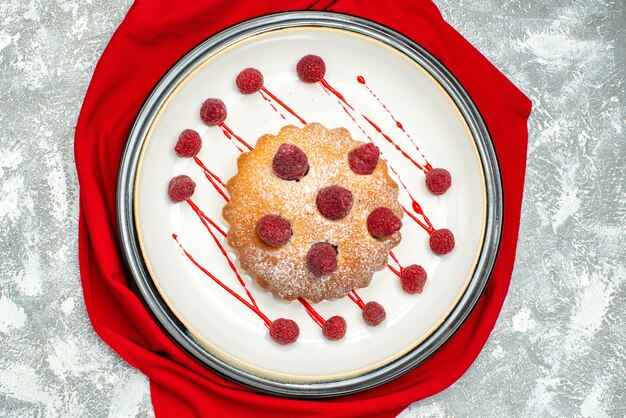 Gâteau aux baies vue de dessus sur plaque ovale blanche châle rouge sur surface grise