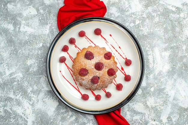 Gâteau aux baies vue de dessus sur plaque ovale blanche châle rouge sur surface grise