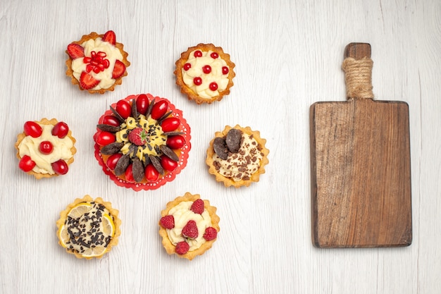 Photo gratuite gâteau aux baies vue de dessus sur les tartes de napperon en dentelle ovale rouge et une planche à découper en bois sur le sol en bois blanc