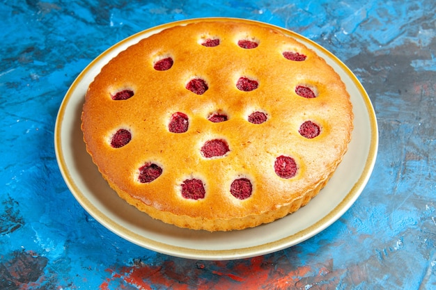 Gâteau aux framboises vue de face sur plaque blanche sur table bleue