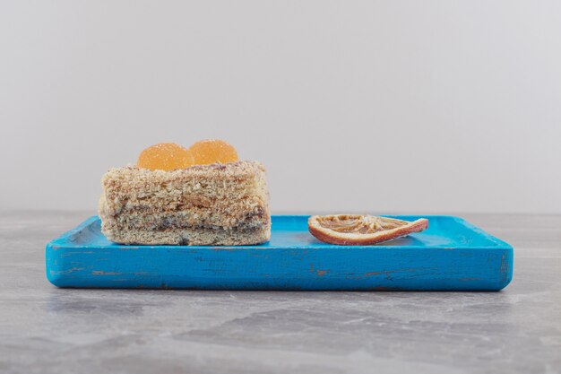 Un gâteau aux marmelades à côté d'une tranche de citron séchée sur un plateau bleu sur marbre