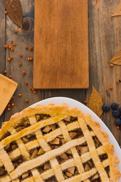 Gâteau aux pommes près de la planche à découper entre le feuillage et les baies