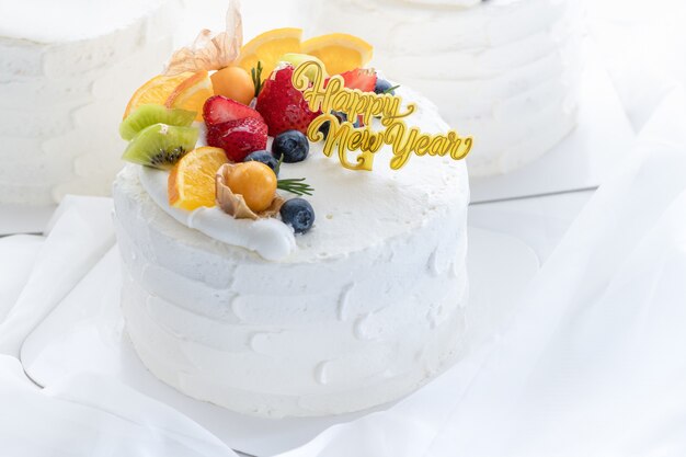 Gateau A La Creme Blanche Avec Bonne Annee Et Garni D Orange De Fraise De Myrtille Et De Groseille Du Cap Sur Fond De Tissu Blanc Espace Copie Et Concept De Dessert