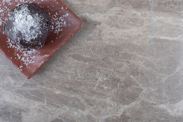 Gâteau enduit de poudre de chocolat et de vanille et pommes de pin sur un plateau sur une surface en marbre