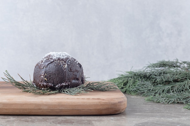 Gâteau enrobé de chocolat, planche de bois et branches de pin sur une surface en marbre