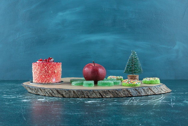 Gâteau, marmelades, beignets et une pomme sur une planche sur bleu.